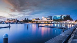 City waterfront at dusk featuring calm water, buildings, and boats at dock.