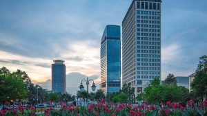 Modern glass office buildings surrounded by landscaped gardens and vibrant flowers at sunrise.