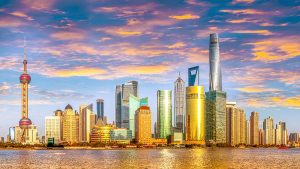 City skyline at sunset with modern skyscrapers and a river in the foreground.