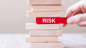 Hand removing a block labeled "RISK" from a stacked wooden game, illustrating concepts of risk management.
