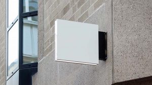 Wall-mounted blank sign attached to a textured building exterior, without visible text or symbols.