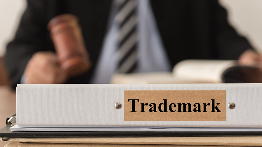 Attorney holding a gavel with a binder labeled "Trademark" in a legal office setting.