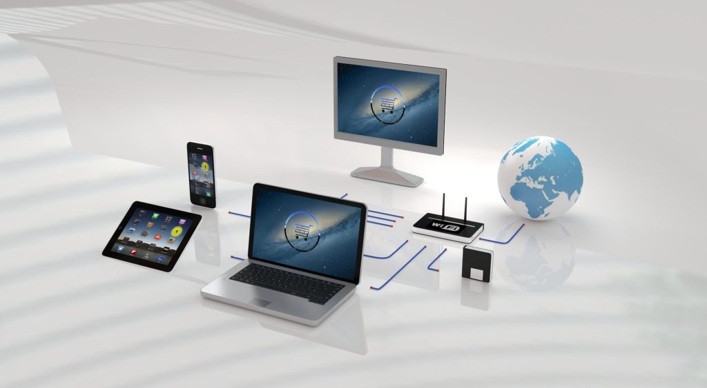 Multiple electronic devices including a laptop, tablet, smartphone, and desktop monitor arranged with a globe and router.