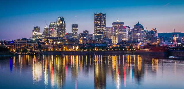 City skyline reflecting on water during twilight, featuring modern buildings and colorful lights.