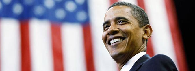 Smiling man in a suit against a backdrop of the American flag.