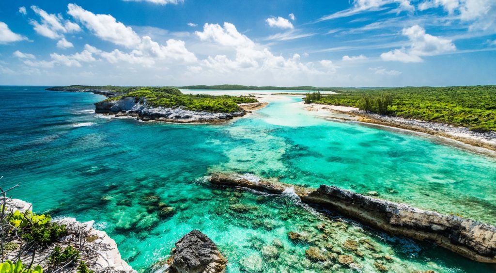 Tropical seascape with turquoise waters, rocky shoreline, and lush green landscapes under a bright blue sky.