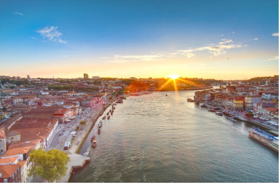 Panoramic view of a river at sunset, surrounded by city buildings and boats along the waterfront.