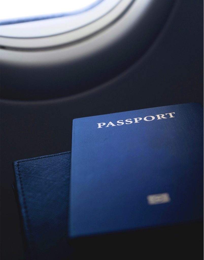 Blue passport placed on a surface near an airplane window, indicating travel context.