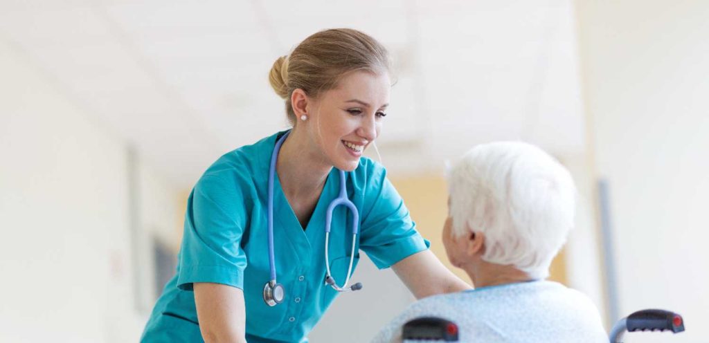 Nurse assisting elderly patient in hospital corridor, demonstrating care and professionalism.