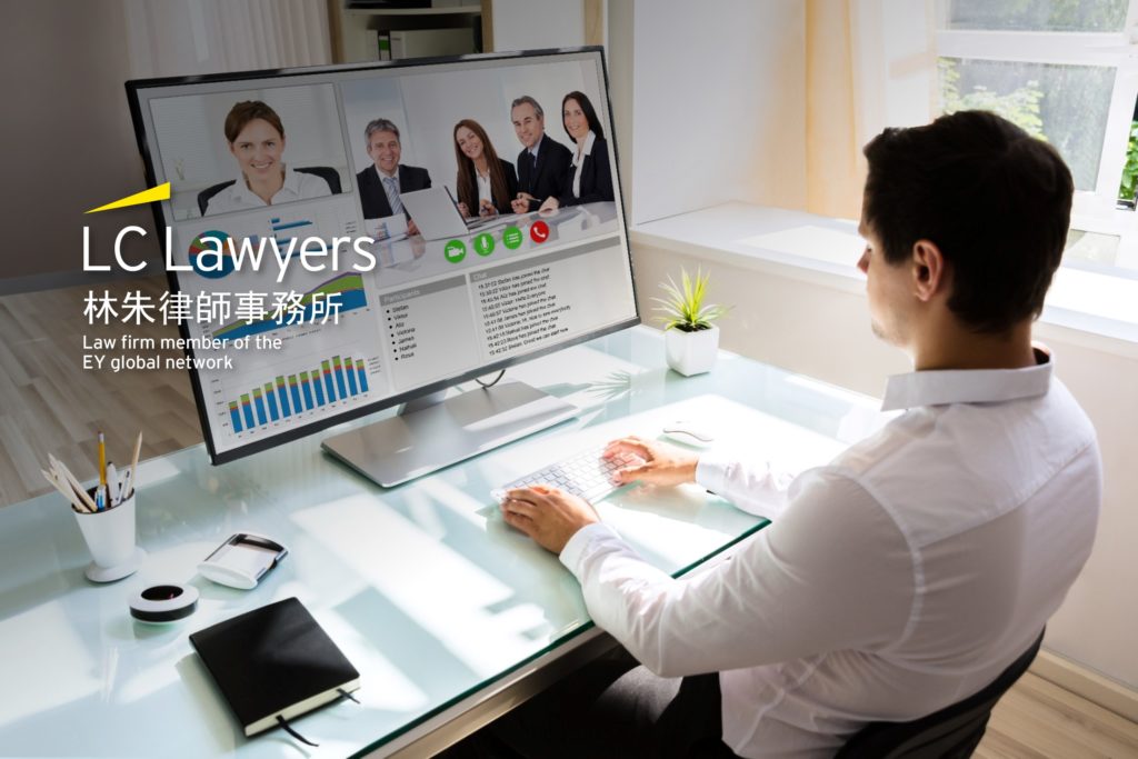 Lawyer participating in virtual meeting with clients, displaying legal documents on a large monitor in an office setting.