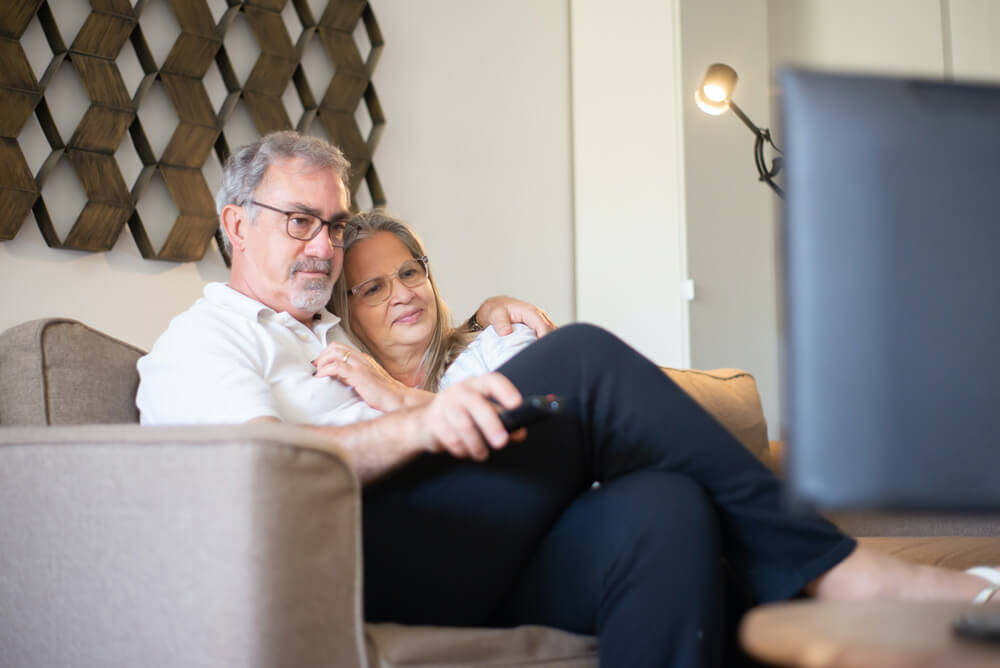 Couple sitting on a couch, watching television and enjoying each other's company in a cozy living room.