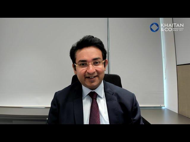 Lawyer smiling while seated in an office setting, with a formal suit and a virtual meeting backdrop.