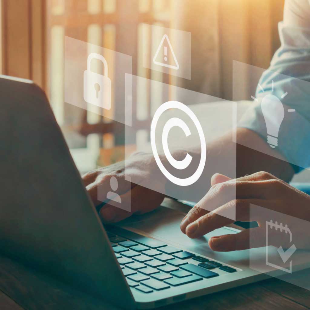 Hands typing on a laptop with digital icons, including copyright symbol and security lock, in a modern workspace.