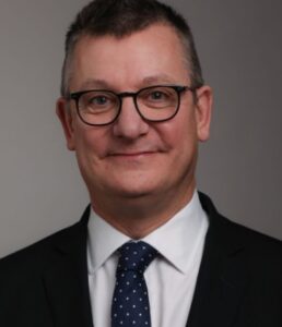 Professional man in black suit and glasses, presenting a confident demeanor, suitable for a legal setting.