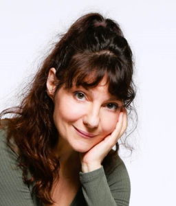 Professional woman with long brown hair resting her chin on her hand, smiling at the camera against a white background.