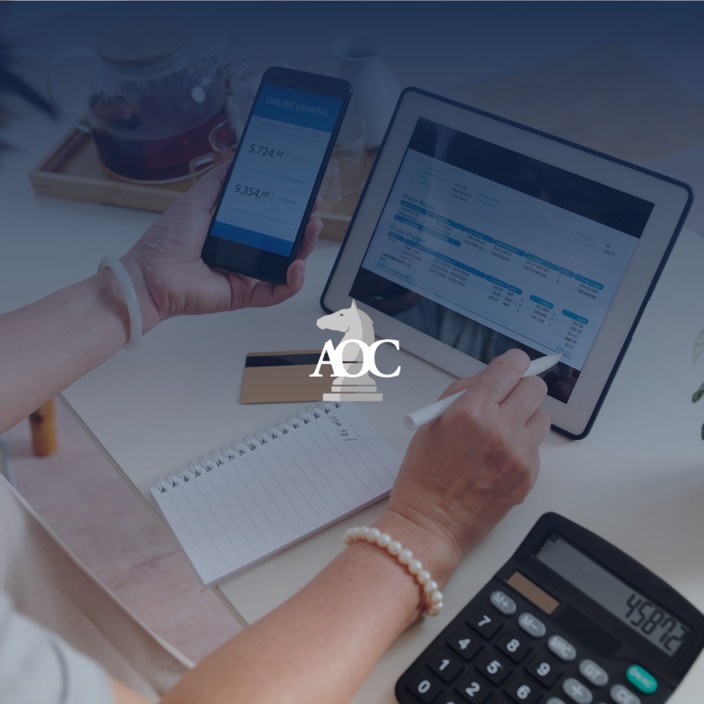 Person reviewing financial data on tablet and smartphone while taking notes on a notepad at a desk.