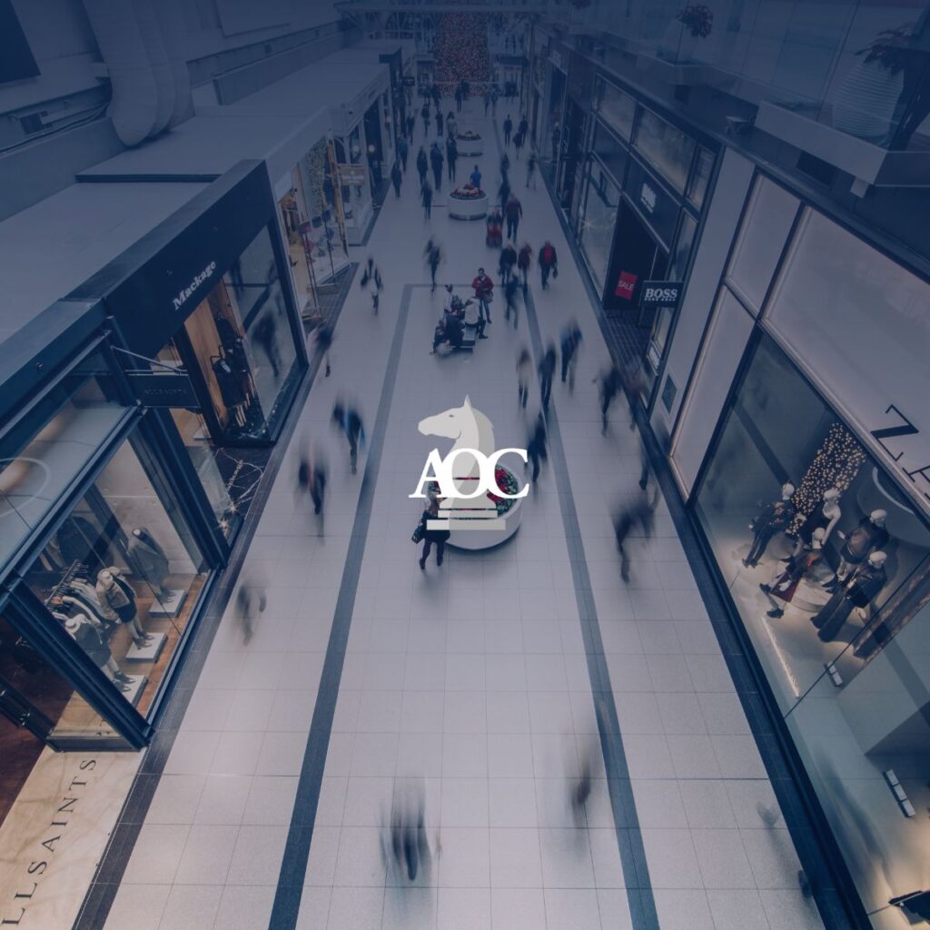 Busy shopping mall interior with blurred pedestrians and retail storefronts lining both sides.