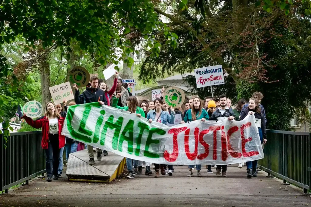 Group of protesters marching with a large banner reading "CLIMATE JUSTICE" and holding various signs in support of environmental activism.