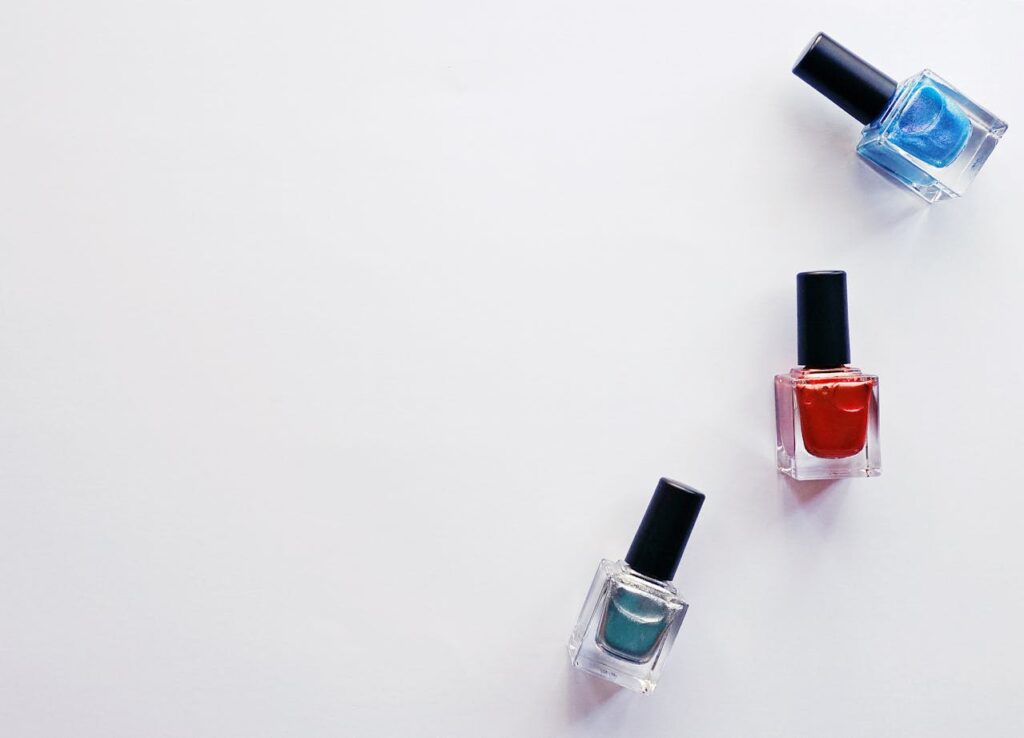 Three nail polish bottles in blue, red, and teal arranged on a plain white background.
