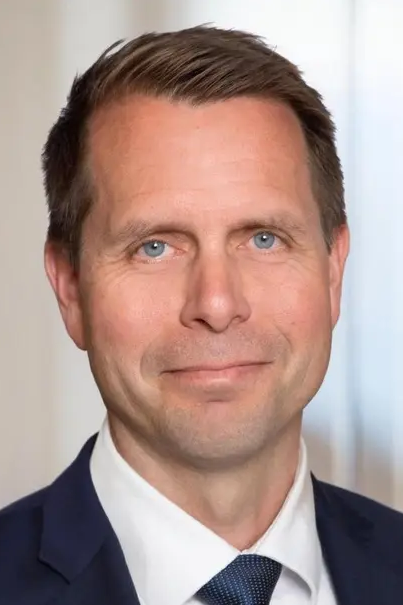 Professional man with short hair and blue eyes, wearing a suit and tie, smiling in a neutral setting.