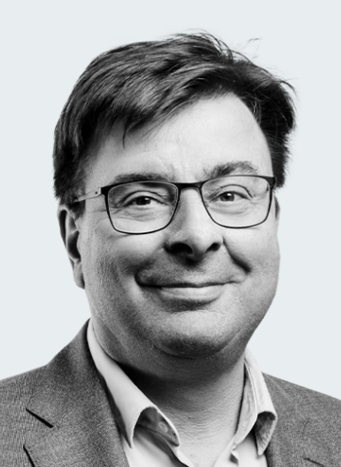 Professional man with glasses and a blazer, smiling against a neutral background.