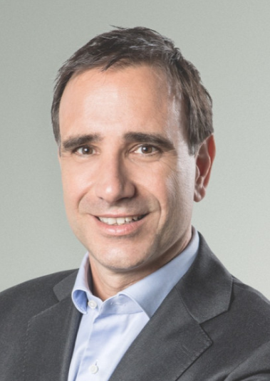 Professional male attorney posing for portrait in a gray blazer and light blue shirt.