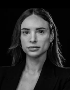 Legal professional with a neutral expression, wearing a blazer, against a dark background.