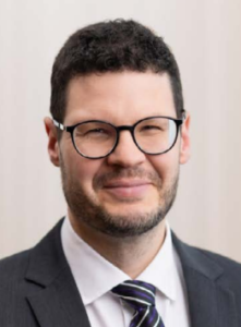 Legal professional with glasses and formal attire, smiling confidently against a neutral background.