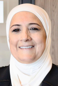 Legal professional smiling in a professional setting, wearing a hijab and a dark suit.