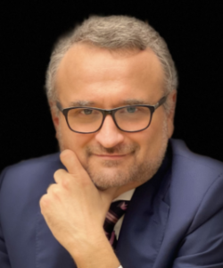Lawyer posing confidently with hand on chin, wearing glasses and a suit, against a dark background.