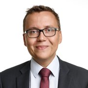 Professional lawyer in a suit and glasses, smiling against a neutral background.