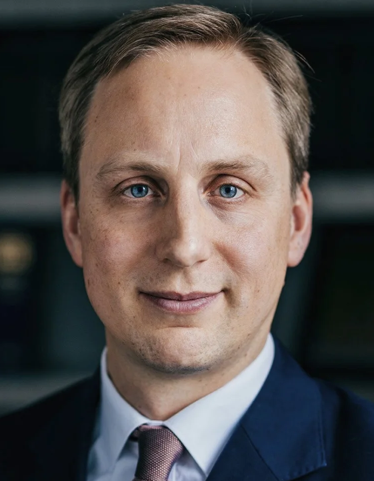 Attorney in formal attire posing confidently with a professional expression against a law office background.