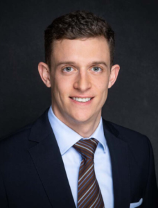 Lawyer in a suit smiling, presenting a professional appearance against a dark background.