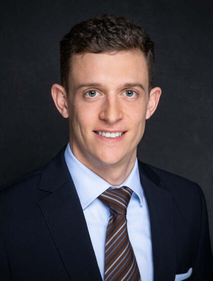 Lawyer in a suit smiling, presenting a professional appearance against a dark background.