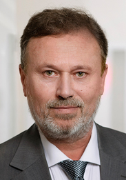 Legal professional with gray hair and beard, wearing a suit, positioned against a neutral background.
