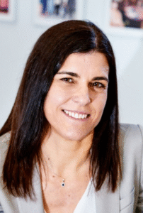Legal professional smiling, wearing a blazer, in an office setting with personal photos in the background.