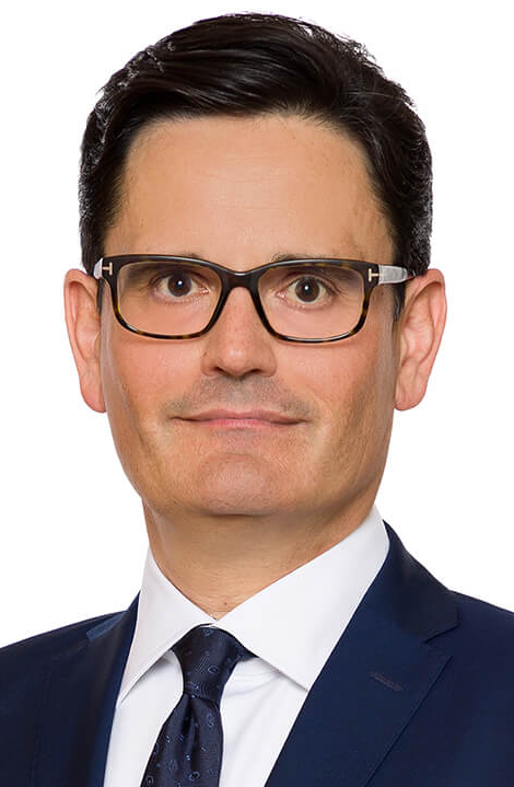 Legal professional in suit and glasses posing for a formal portrait against a neutral background.