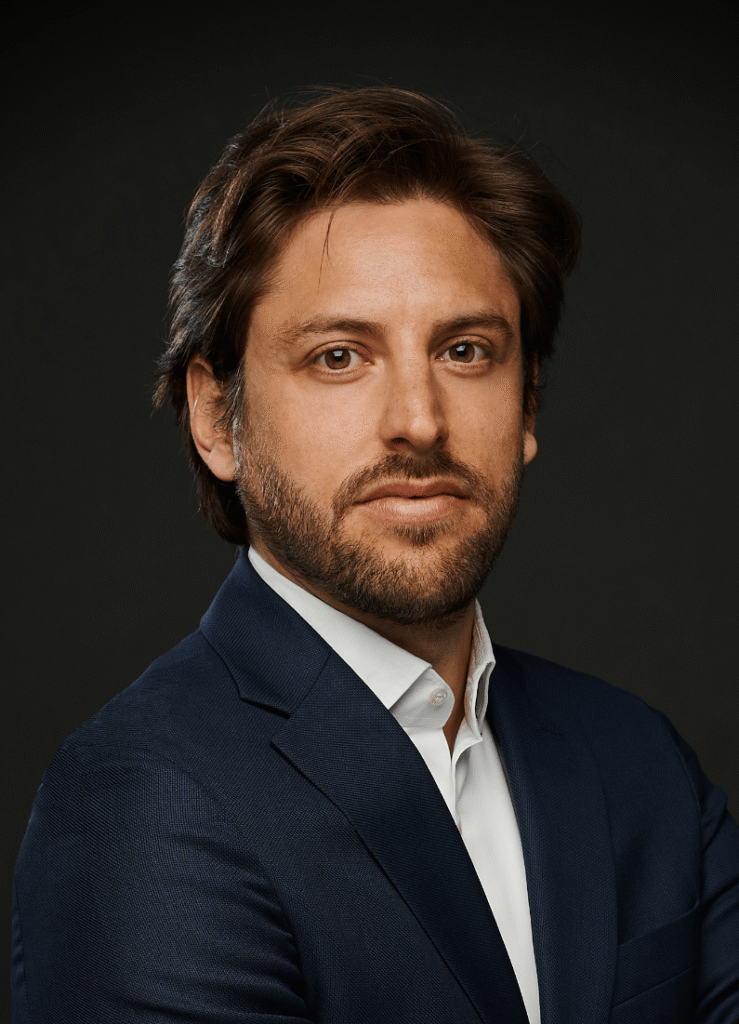 Lawyer in a dark suit, looking directly at the camera, against a plain dark background.
