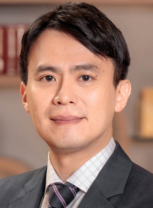 Legal professional with short dark hair and suit, smiling in a law office setting with books in the background.