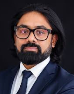 Lawyer posing confidently in formal attire, with dark hair and glasses against a neutral background.