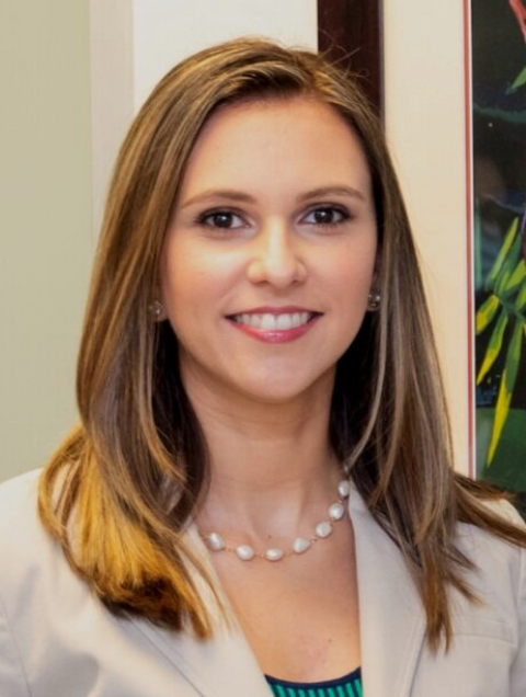 Female attorney posing in a professional setting, wearing a blazer and pearl necklace.