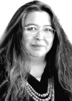 Legal professional with long hair and glasses, smiling, wearing a black shirt and beaded necklace.