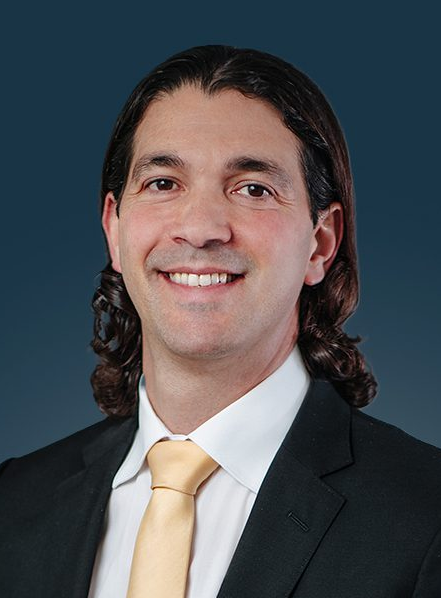 Attorney with long hair wearing a suit and yellow tie, smiling against a dark background.
