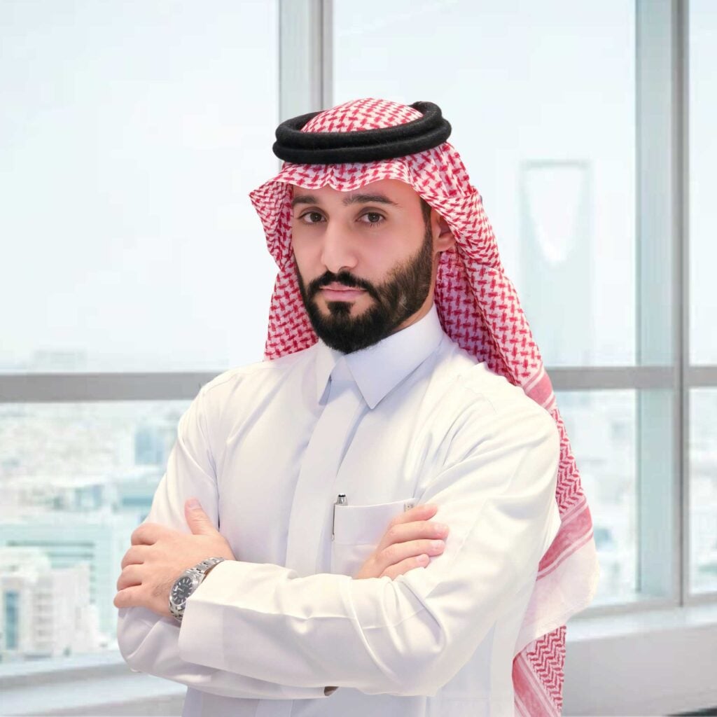 Business professional in traditional attire standing confidently with arms crossed in a modern office setting.