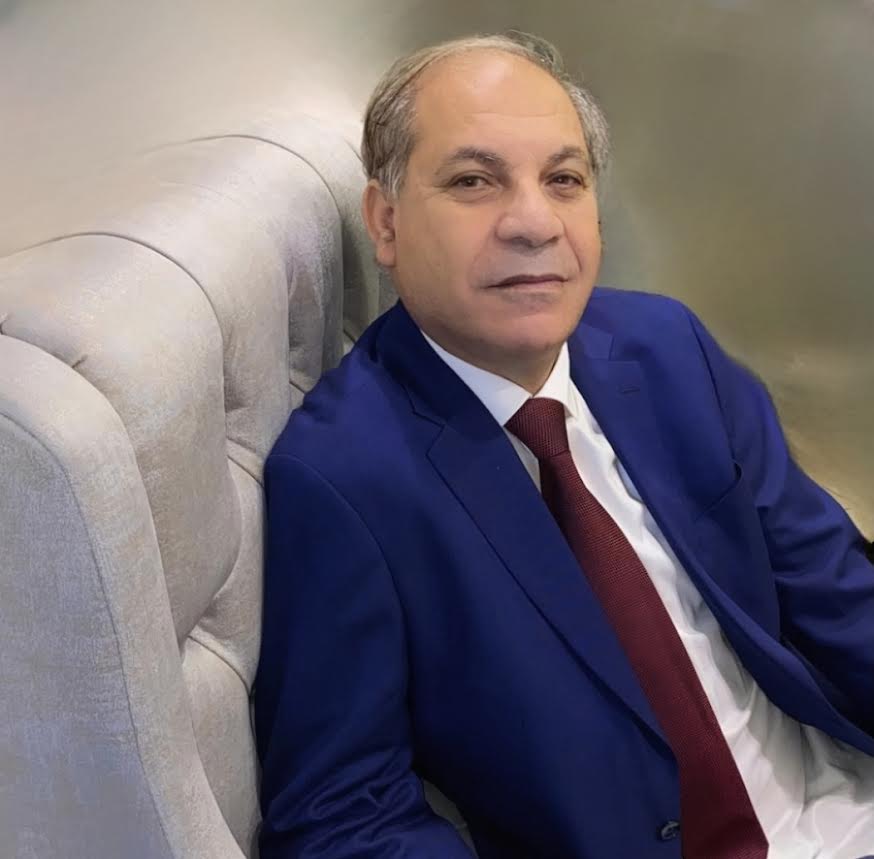 Attorney seated in office, wearing a blue suit and red tie, with a neutral expression.