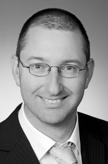 Smiling lawyer in a suit with glasses, posing against a plain grey background.