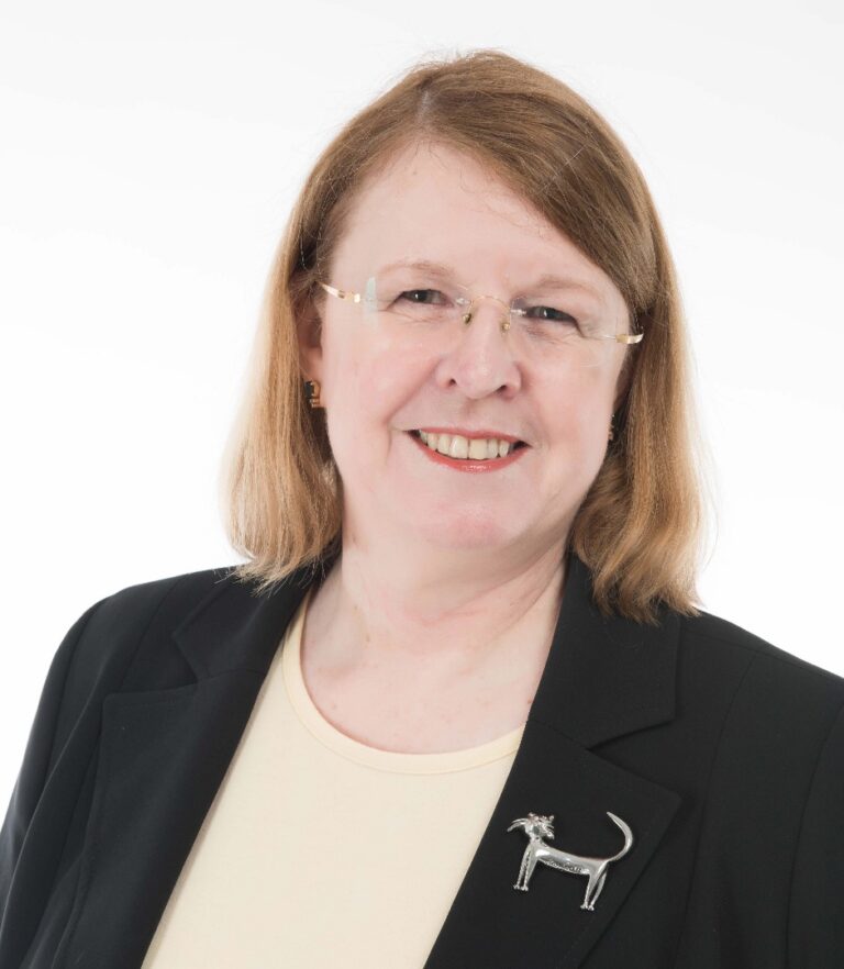 Lawyer smiling in professional attire, wearing a distinctive silver dog brooch against a light background.