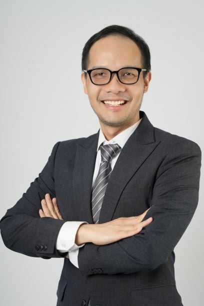 Lawyer smiling confidently with arms crossed, wearing a suit and glasses against a neutral background.