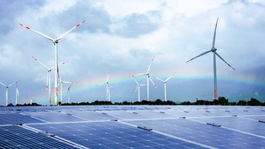 Wind turbines and solar panels in a renewable energy field with a rainbow in the background.