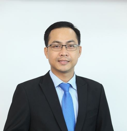 Lawyer in a suit with glasses, standing against a plain background, presenting a professional appearance.